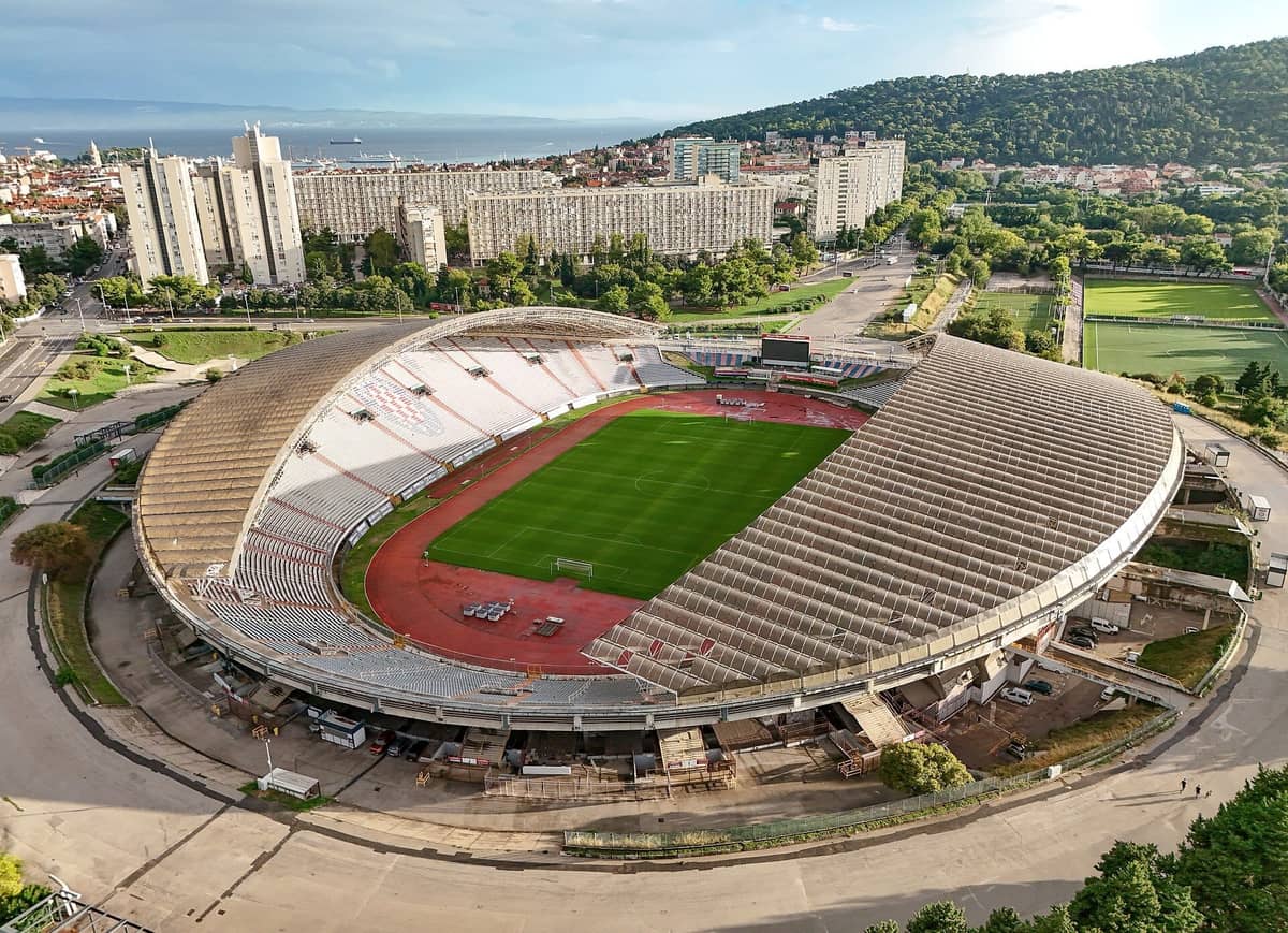 Luftaufnahme des Stadions Poljud in Split, Kroatien, mit seiner ovalen Struktur, grünem Fußballfeld, umliegenden Apartmentgebäuden und nahegelegenen Hügeln bei Tageslicht.