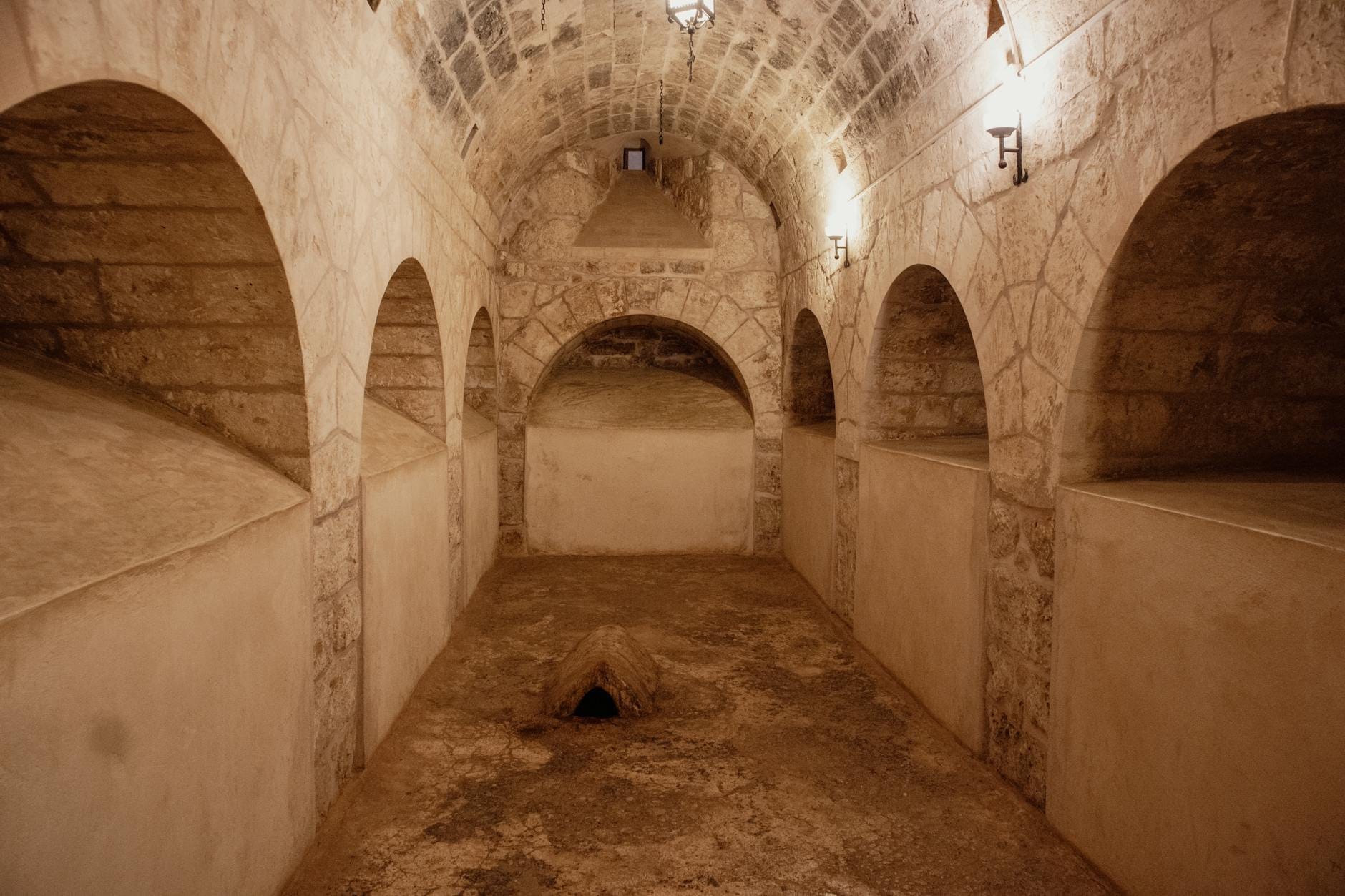 Vista interna di un'antica camera funeraria in pietra con nicchie ad arco e soffitto a volta, illuminata in modo tenue per un effetto sotterraneo suggestivo.