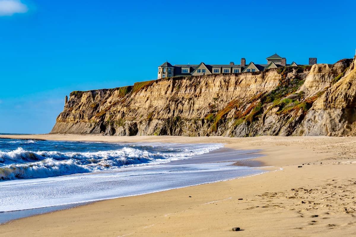 Costa de Half Moon Bay con acantilados, playa de arena y el hotel Ritz-Carlton sobre el promontorio bajo un cielo azul despejado.