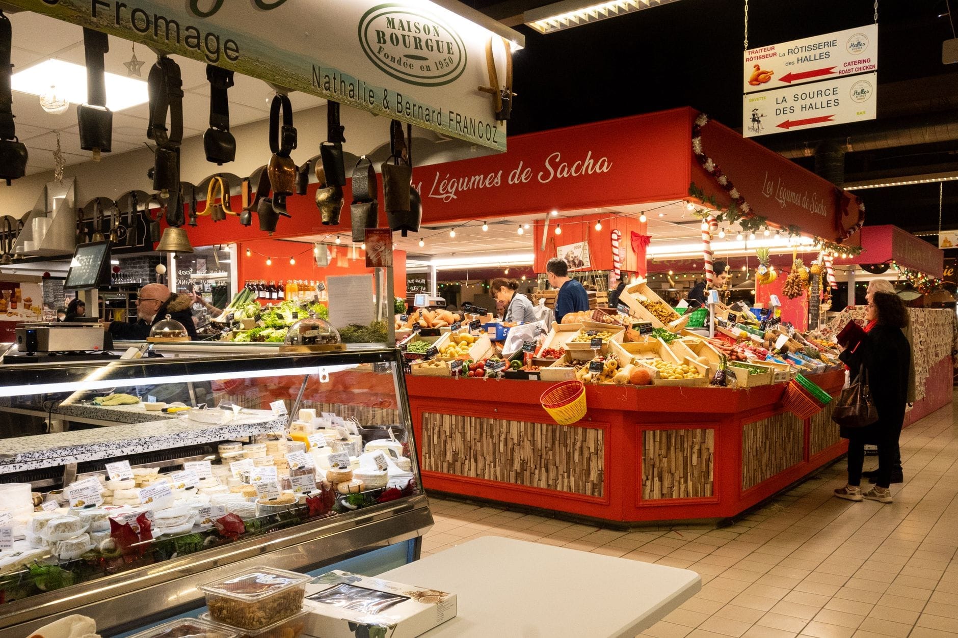 All'interno del mercato Halles Centrales a Le Havre, bancarelle colorate di prodotti freschi e un bancone del formaggio sono esposti sotto una brillante illuminazione interna con acquirenti in giro.
