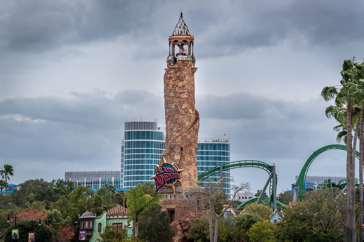 Torre faro de Universal Orlando Islands of Adventure con montaña rusa del parque y edificios del resort al fondo bajo un cielo nublado