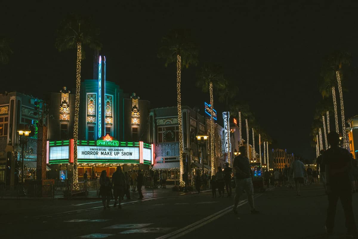 Calle de Universal Studios Florida de noche, iluminada con luces de neón y palmeras, personas caminando, marquesina de cine brillando.
