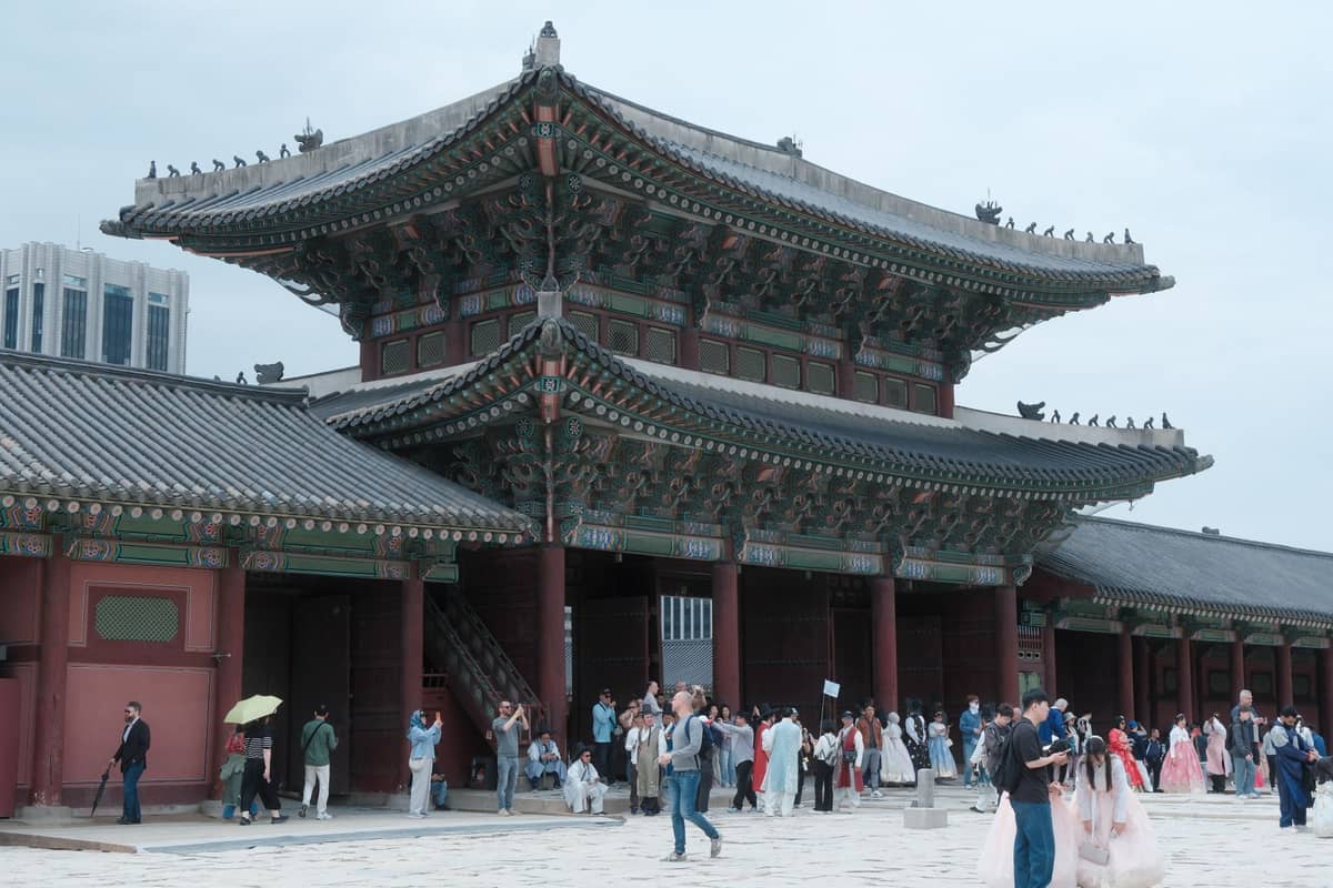 Multidão em frente ao portão principal do Palácio Gyeongbokgung em Seul, com pessoas vestindo hanbok coloridos