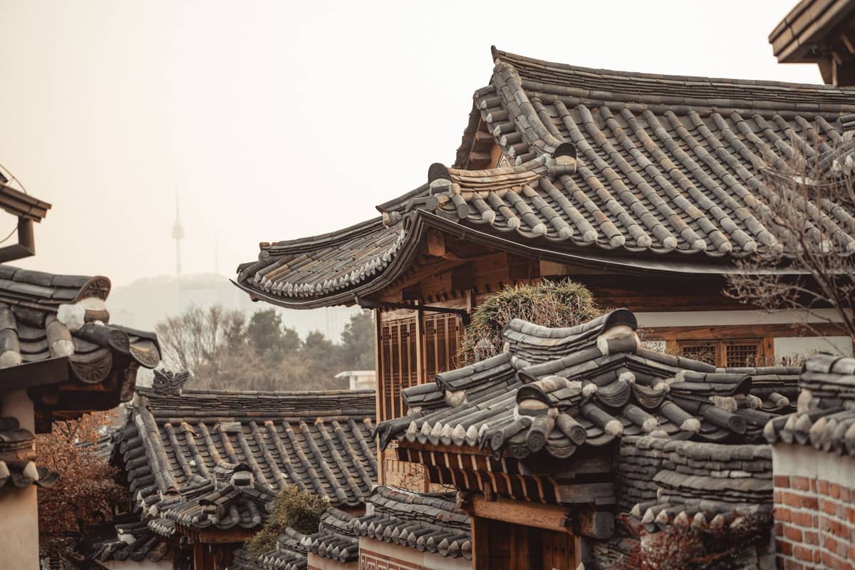 Telhados de casas hanok coreanas tradicionais no Bukchon Hanok Village de Seul com a Torre Namsan ao fundo em um dia enevoado.