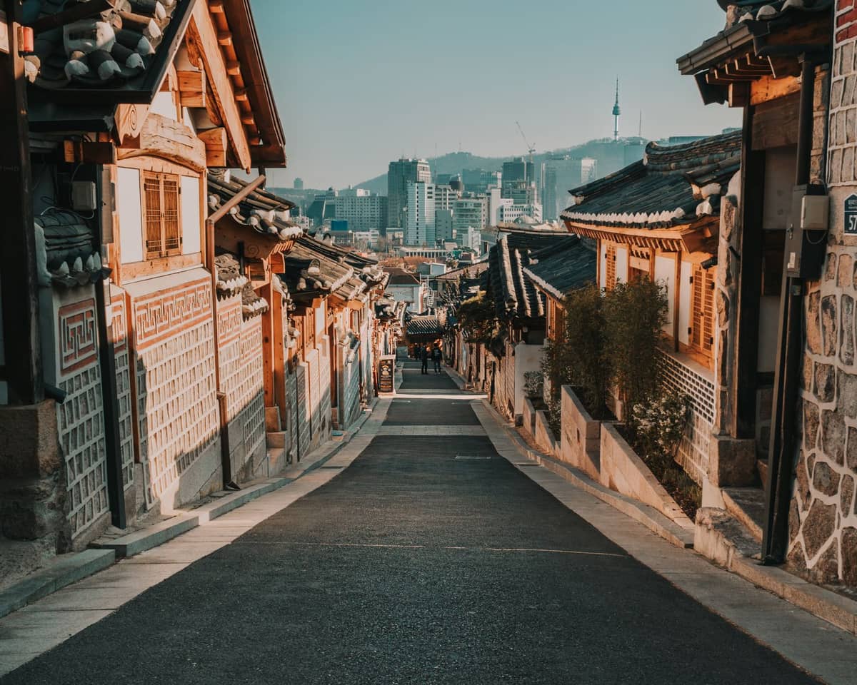 Vista panorâmica da rua principal da Vila Hanok de Bukchon, em Seul, com casas tradicionais coreanas alinhadas e a Torre Namsan ao fundo.