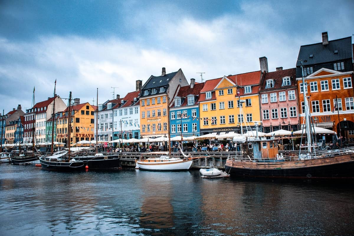 Edifici storici colorati e barche ormeggiate costeggiano il canale di Nyhavn a Copenaghen sotto un cielo nuvoloso.