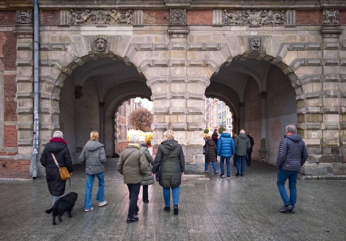 Un gruppo di persone in un tour guidato a piedi che attraversa uno storico portale ad arco in pietra a Copenaghen.