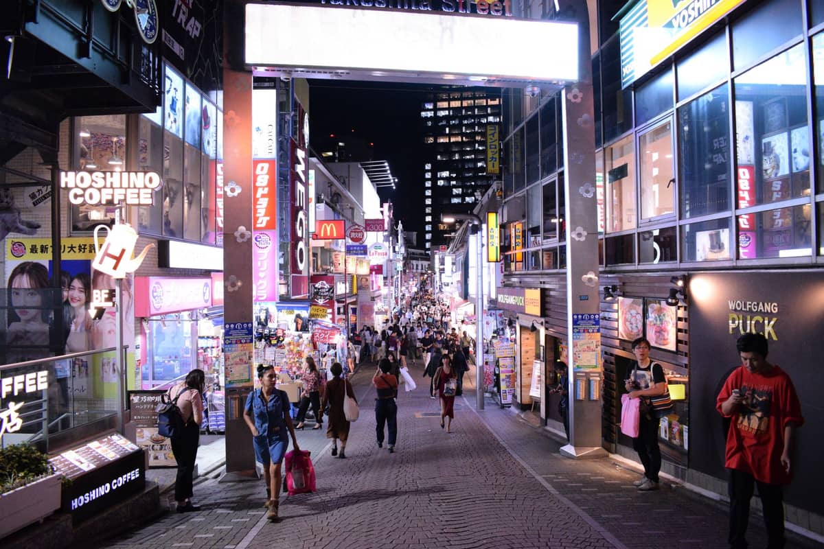 Takeshita Street in Harajuku at night, bustling with people, bright shop signs, and colorful lights in a vibrant pedestrian shopping area.