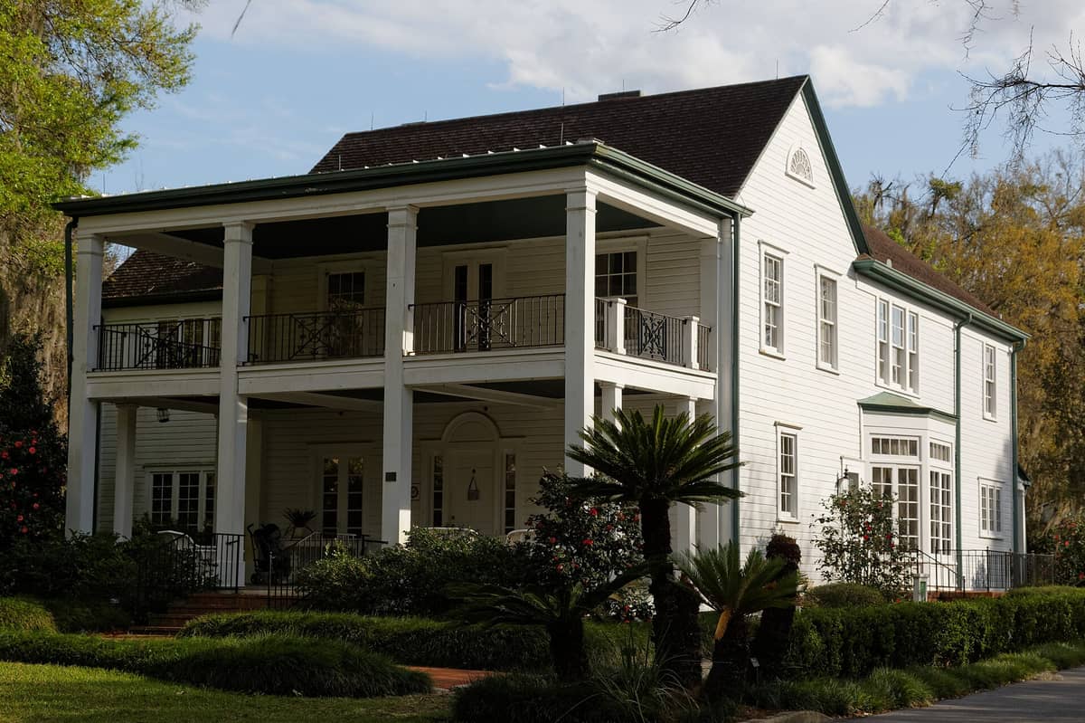 The historic 1888 house museum at Harry P. Leu Gardens, a two-story white wooden home with a large porch, surrounded by lush subtropical landscaping.