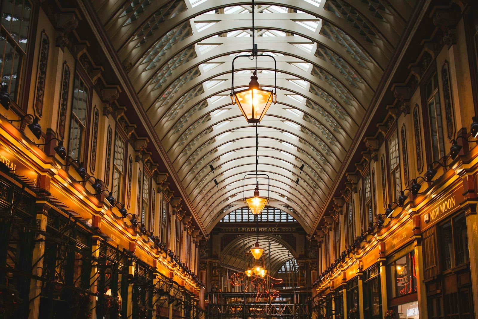 Vista interior do Leadenhall Market em Londres, com teto ornamentado de vidro, iluminação aconchegante e arquitetura histórica usada como locação de filmagem de Harry Potter.
