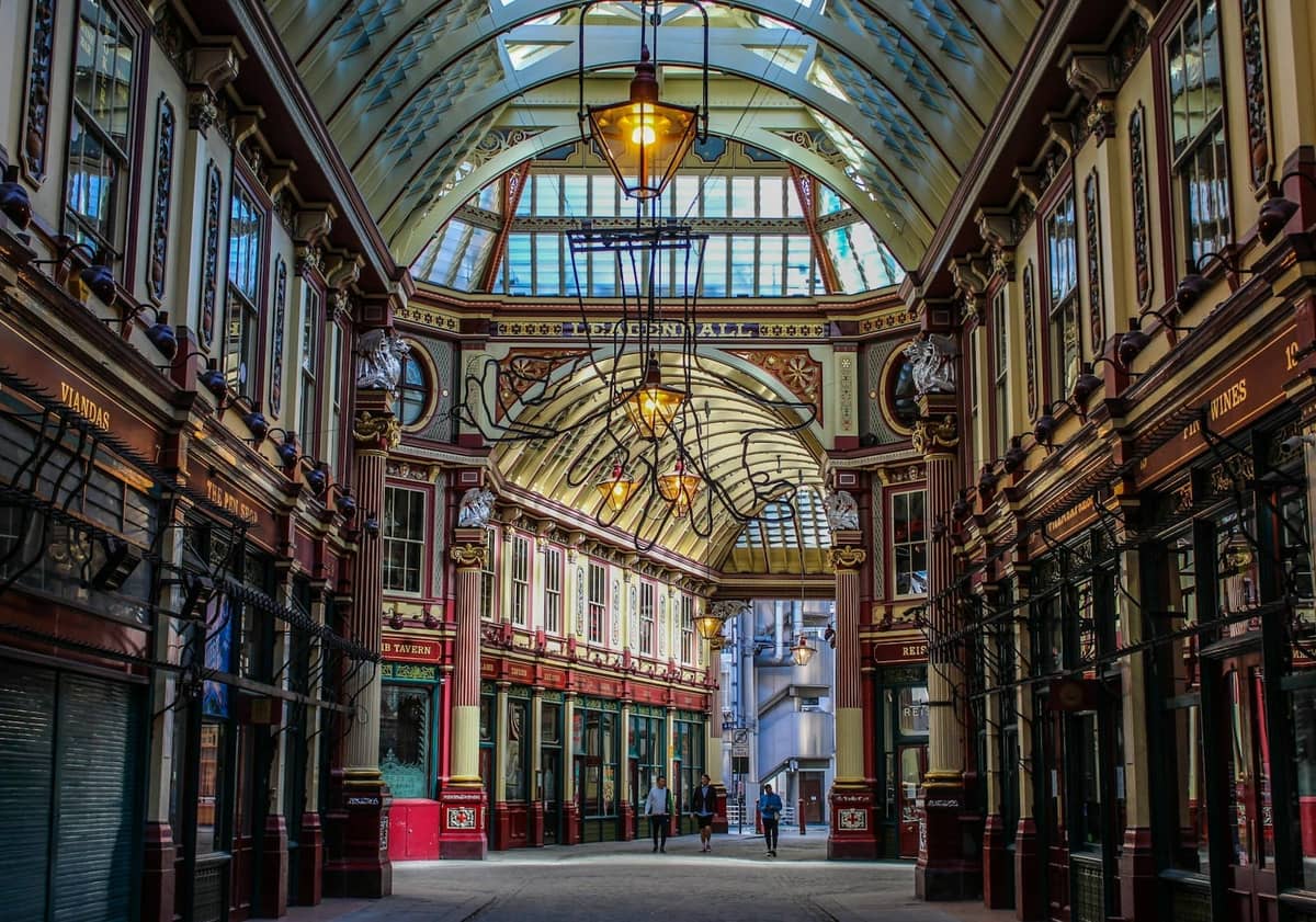 Vista da passagem coberta ornamentada do Leadenhall Market com teto verde e bordô, lampiões vintage e fachadas decorativas de lojas em Londres.
