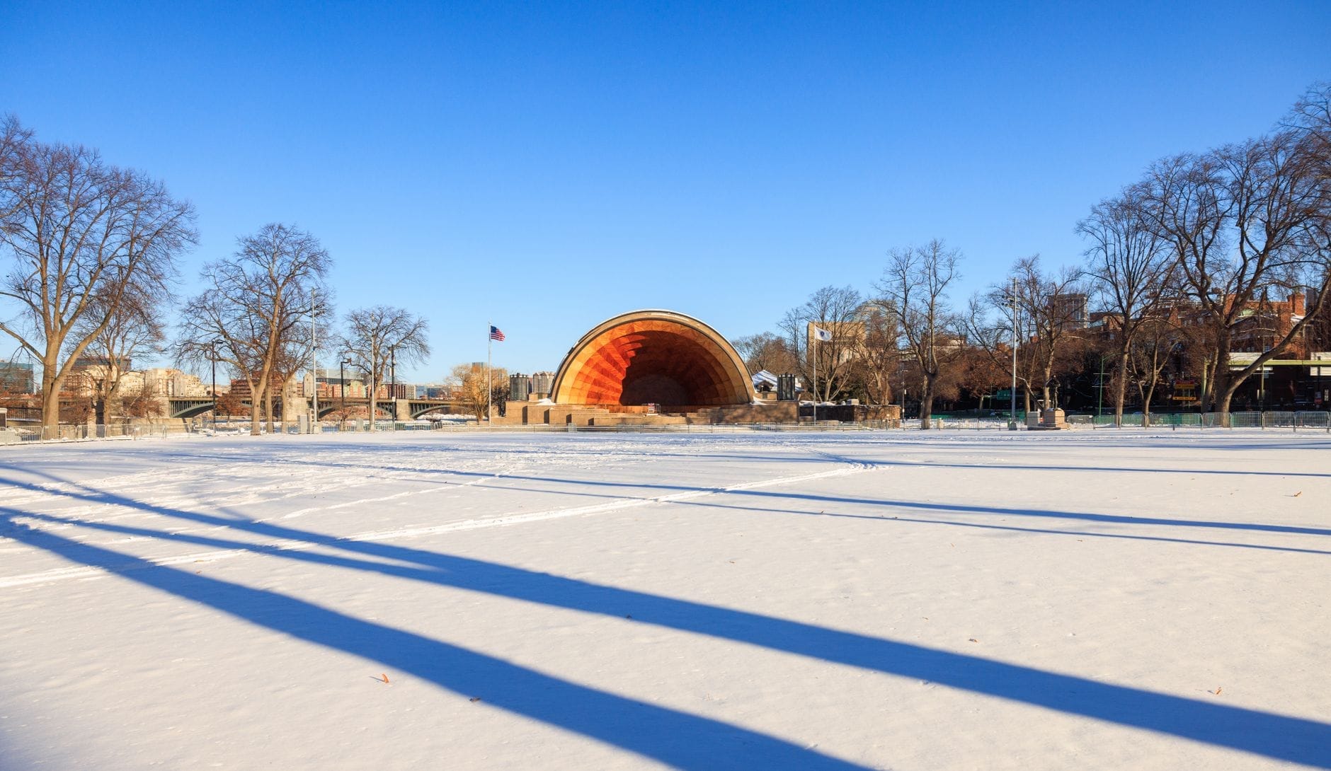 Vista ampia dell'anfiteatro Hatch Memorial Shell in una limpida giornata invernale, con la neve che copre il suolo e il cielo azzurro sopra.