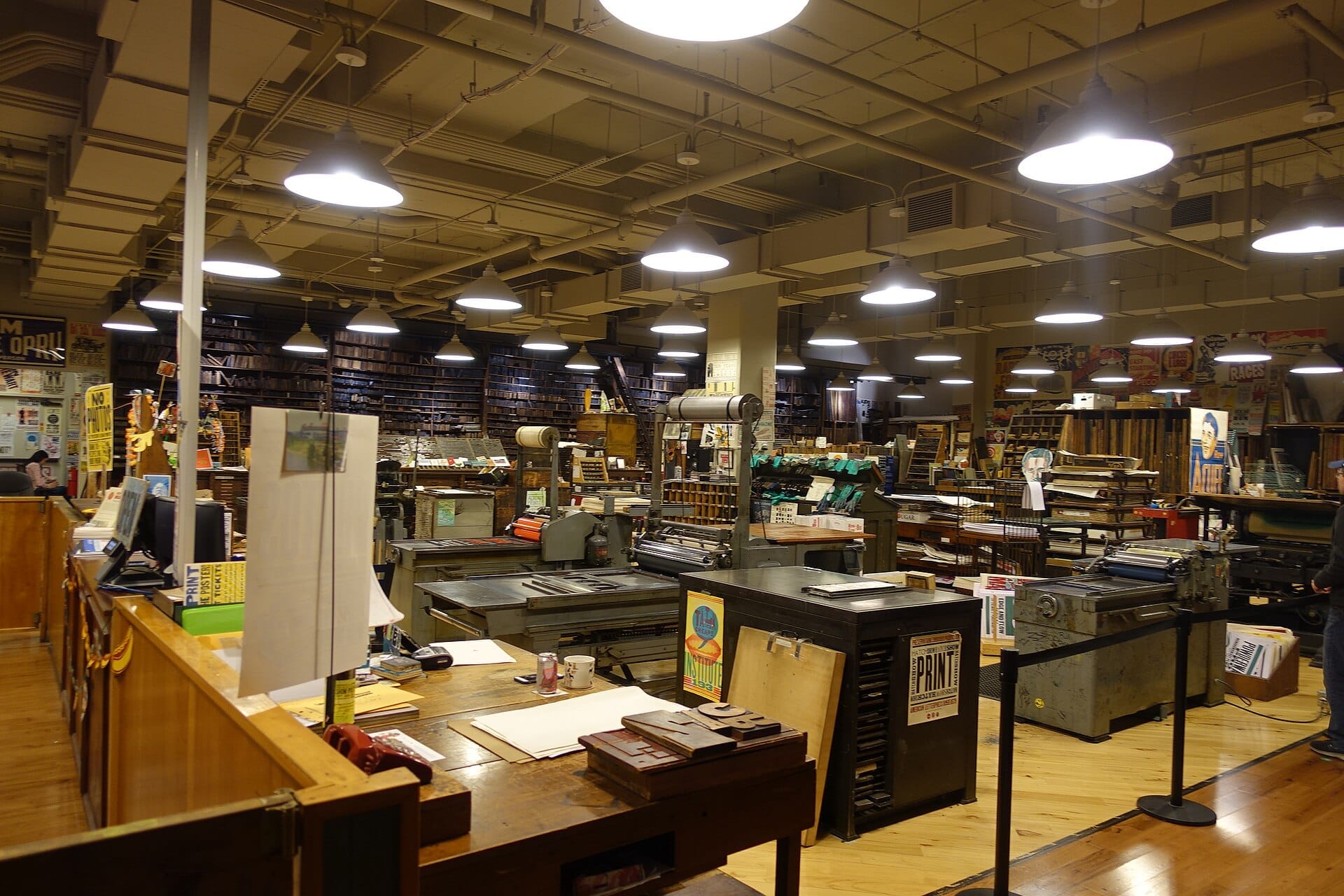 Vista interior de Hatch Show Print en Nashville, con máquinas de impresión tipográfica vintage, suelos de madera e iluminadas luces industriales en el techo.