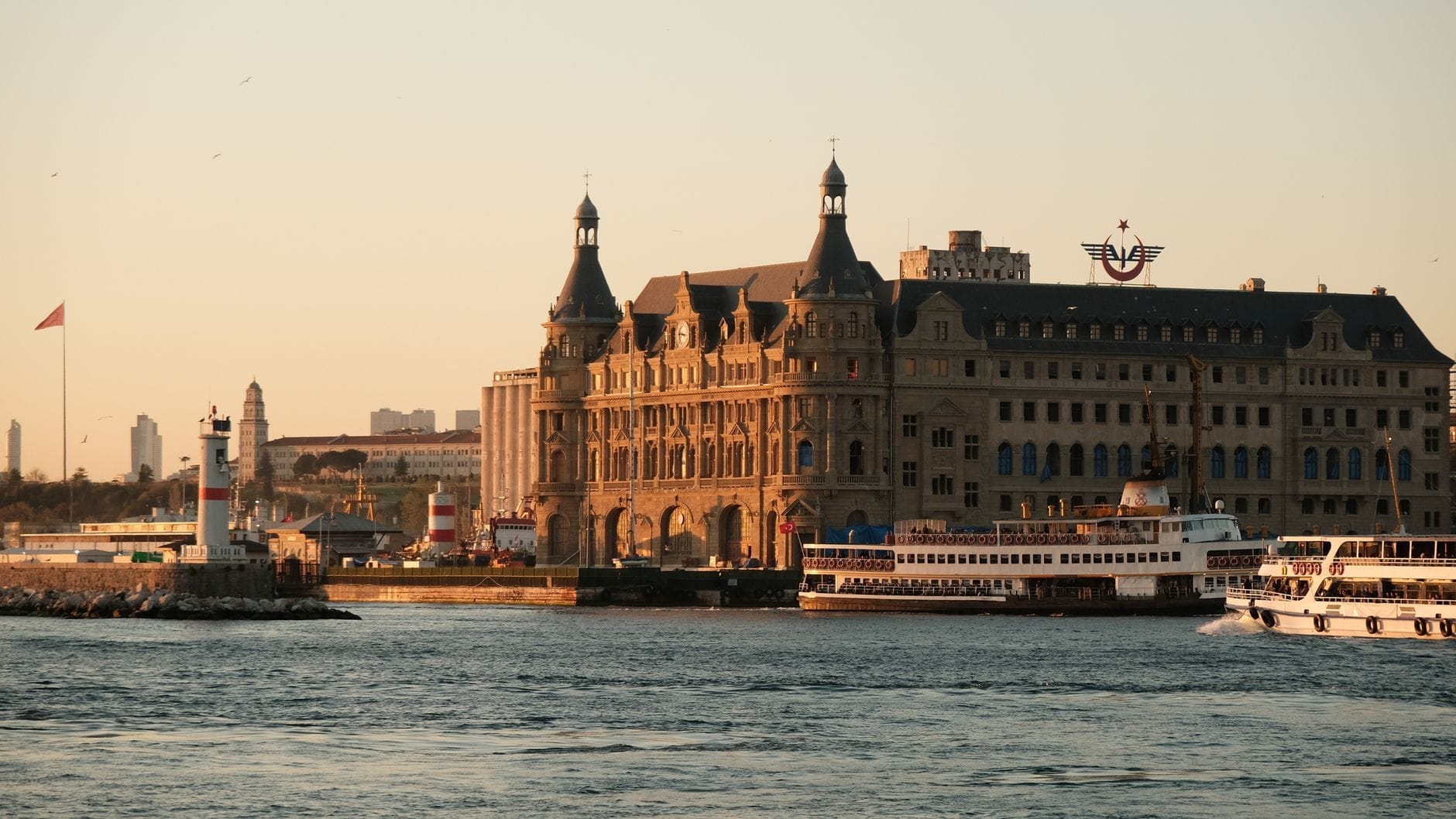 La stazione di Haydarpaşa all'ora d'oro, con la luce calda del tramonto sulla facciata neo-barocca, i traghetti in primo piano e le acque del Bosforo che rispecchiano lo storico edificio.