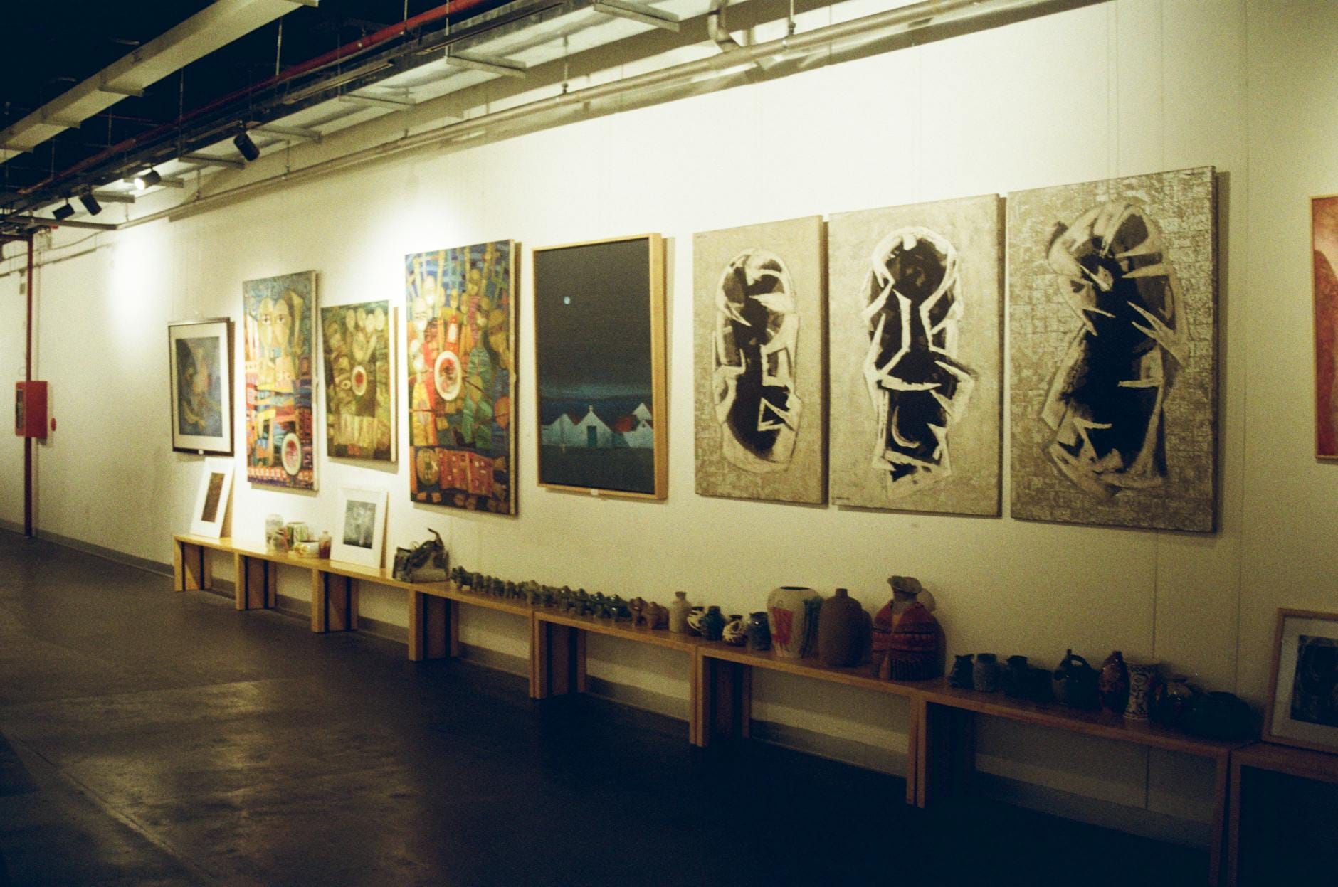 Obras de arte vietnamita contemporáneo y cerámica exhibidas a lo largo de una pared bien iluminada, mostrando la creatividad moderna en un acogedor espacio expositivo.