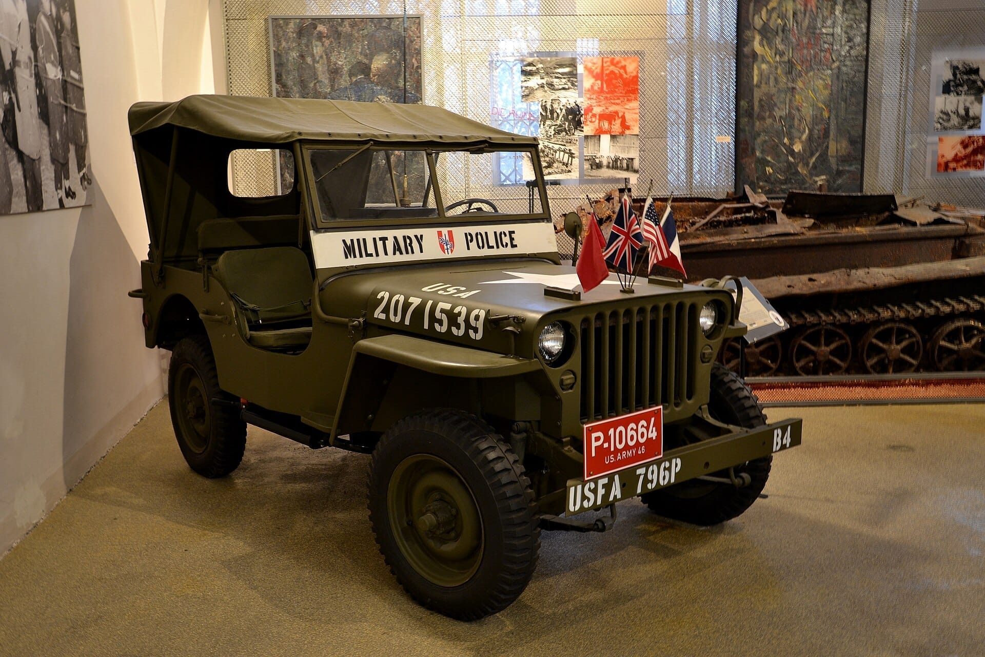 Klassischer Militärpolizei-Jeep im Heeresgeschichtlichen Museum Wien, mit Fahnen und historischen Panzern im Hintergrund unter Museumsbeleuchtung.