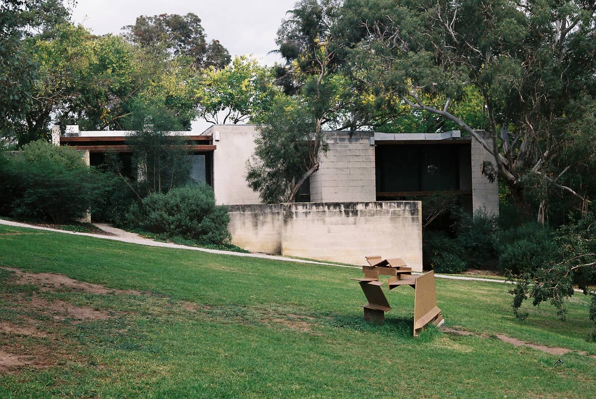 Blick auf das Heide Museum of Modern Art: ein modernistisches Betongebäude inmitten grüner Rasenflächen und Bäume, im Vordergrund eine Außenskulptur.