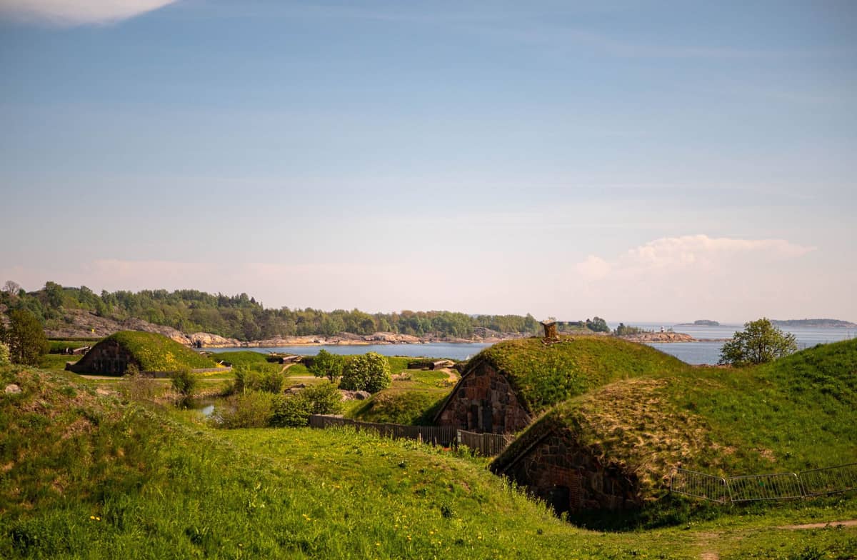 Vista sobre as fortificações cobertas de grama da ilha de Suomenlinna, com o Mar Báltico e o arquipélago de Helsinque ao fundo em um dia ensolarado.