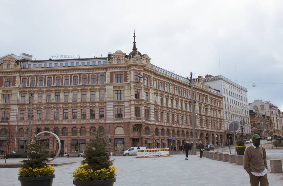 Elegante edifício histórico com a placa Vasateatteri no centro de Helsinki, pessoas caminhando em uma praça da cidade, dia nublado de primavera ou outono.