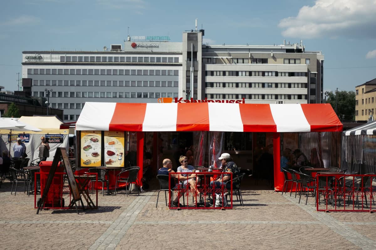 Barraca de mercado ao ar livre com toldo vermelho e branco e pessoas sentadas em mesas no centro de Helsinque