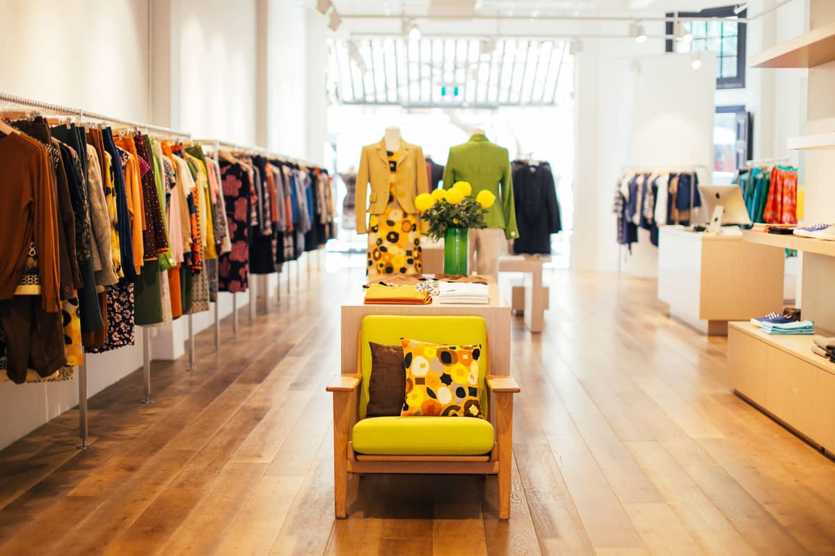 Boutique brilhante e elegante em Helsinki exibindo o ousado design finlandês: cadeira mid-century, roupas estampadas e interior de madeira clara.