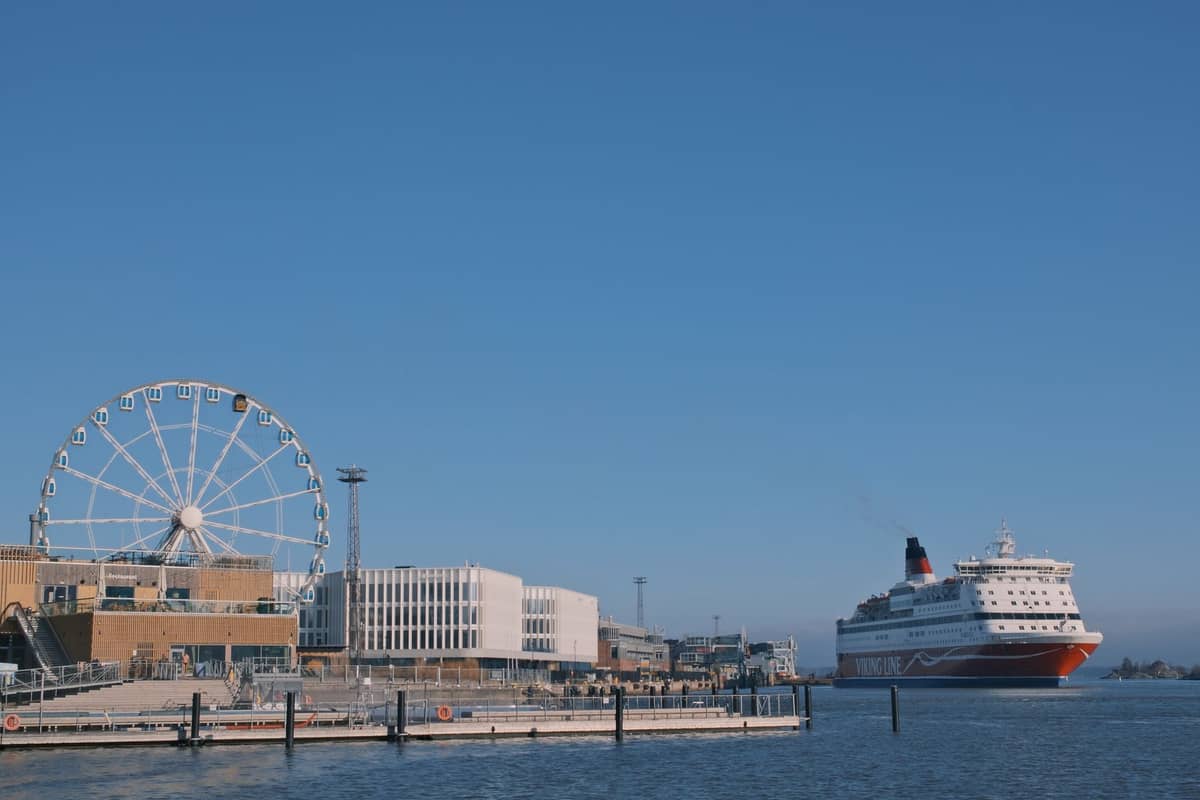 Grande ferry atracado no porto de Helsinki, com o SkyWheel Helsinki e edifícios modernos ao fundo num dia de céu limpo