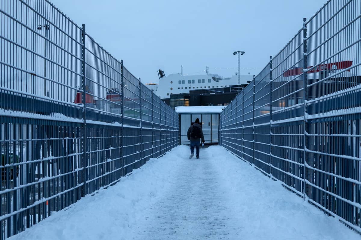 Pessoa caminhando em direção a um terminal de ferry coberto de neve com um grande navio ferry atracado à frente em um dia de inverno em Helsinki.