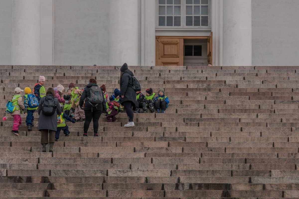 Crianças e adultos em roupas de inverno se reúnem nos degraus de pedra da Catedral de Helsinque, um famoso ponto turístico de Helsinque.