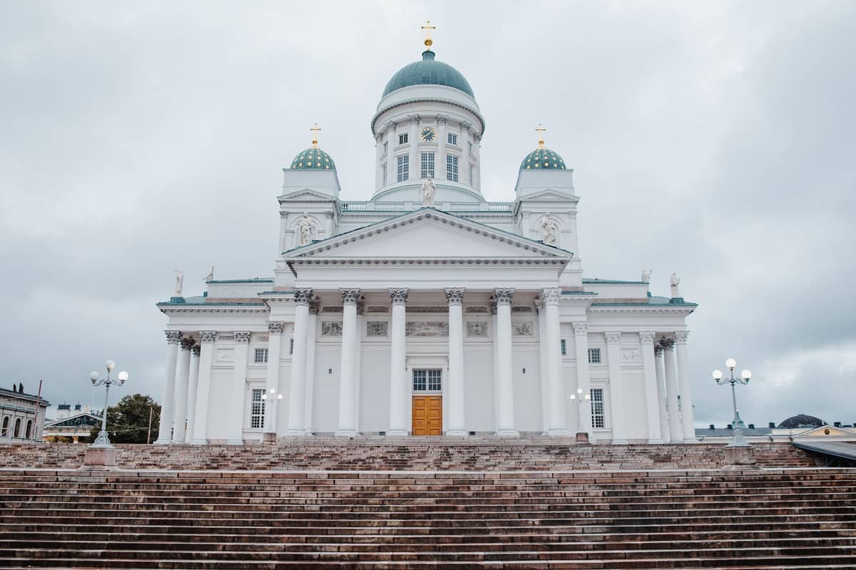 Vista ampla da Catedral de Helsinque acima dos degraus da Praça do Senado sob um céu nublado, um cartão-postal clássico dos roteiros a pé pela cidade.