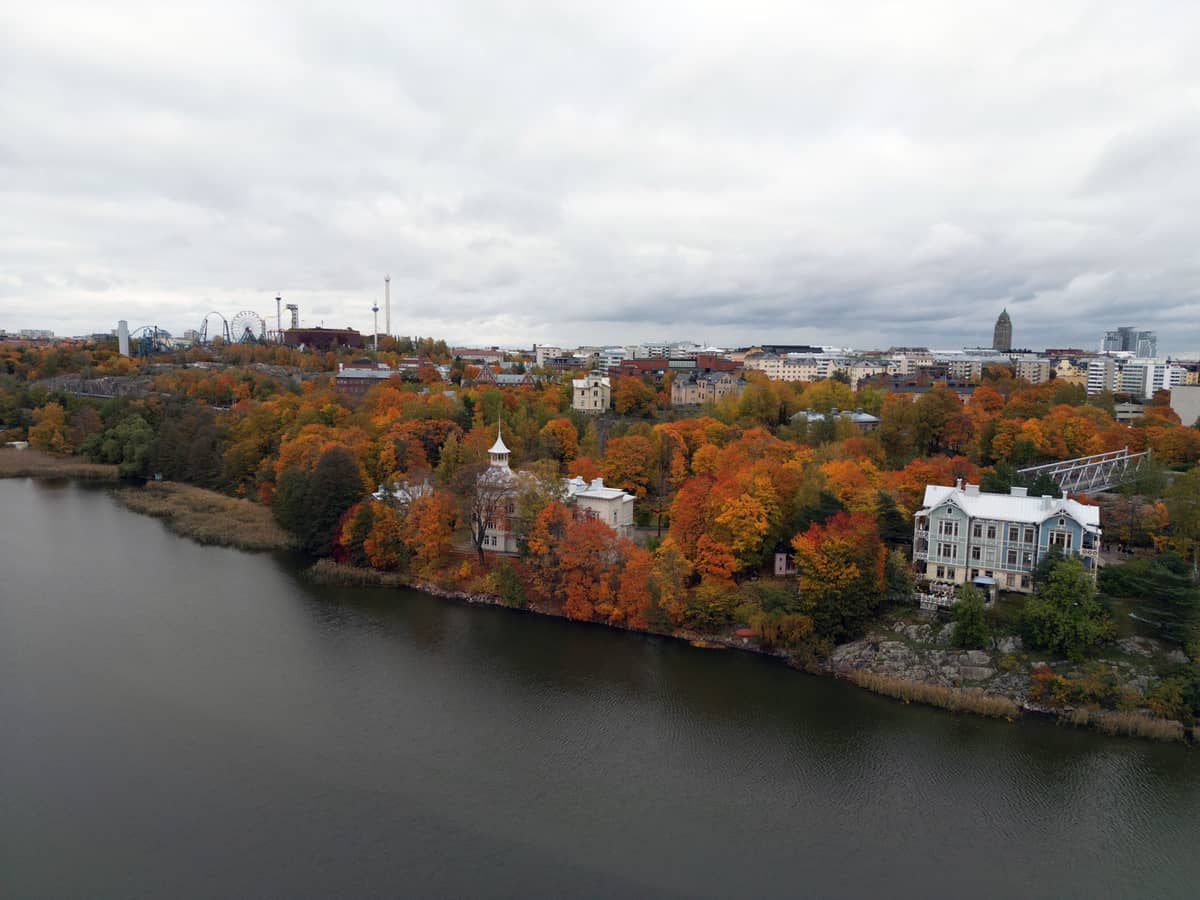Vista aérea da orla de Helsinki no outono, com árvores coloridas de outono, edifícios históricos e o horizonte da cidade sob um céu nublado.