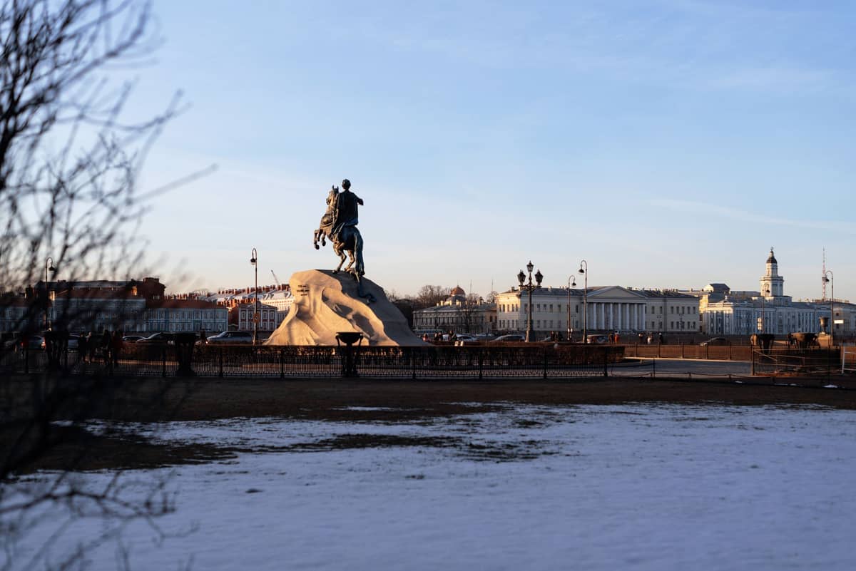 Praça coberta de neve com estátua equestre em frente a edifícios clássicos sob um céu de inverno em Helsinki.
