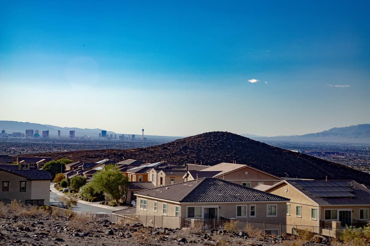Suburban homes in Henderson, Nevada with desert hills in foreground and Las Vegas Strip visible in the distance under a bright blue sky.