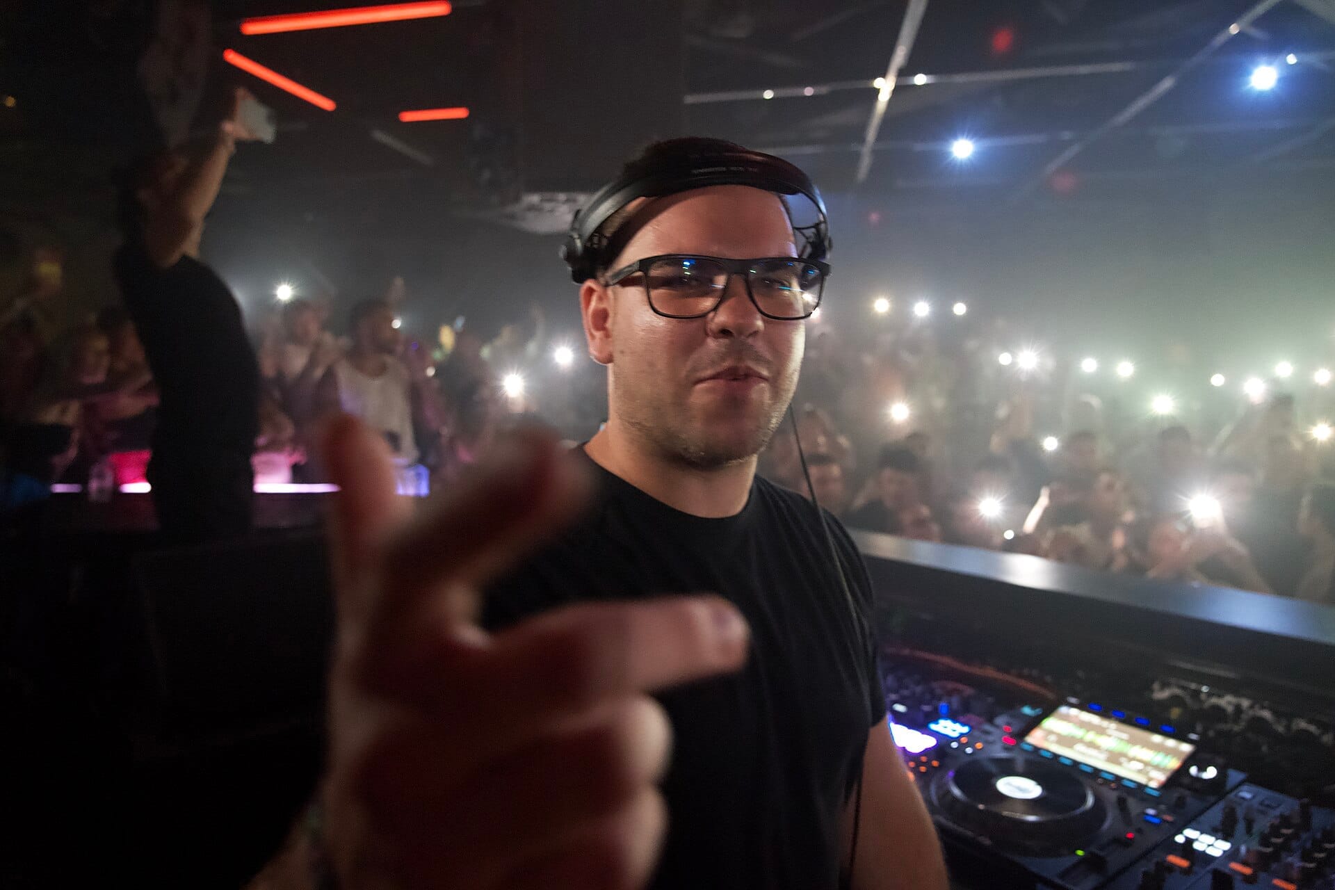 Un DJ si esibisce davanti a una folla vivace all'Hï Ibiza, con luci lampeggianti e attrezzatura per musica elettronica visibile su una pista da ballo buia e affollata.