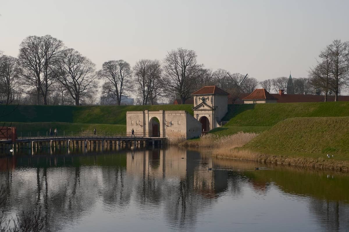 Fosa z trawiastymi brzegami i historyczną bramą fortecy Kastellet w Kopenhadze w słoneczny dzień.