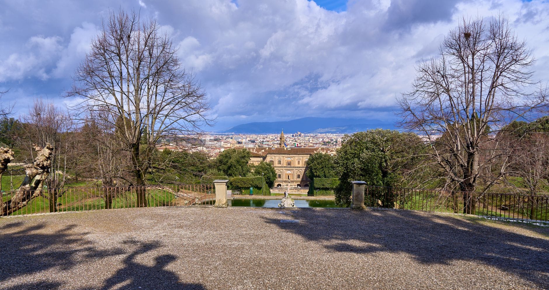 วิวจากสวนลับในเมือง Florence พร้อมทัศนียภาพเมืองแบบพาโนรามา ต้นไม้ และอาคารที่อยู่ไกลออกไปใต้ท้องฟ้าที่มีเมฆมาก