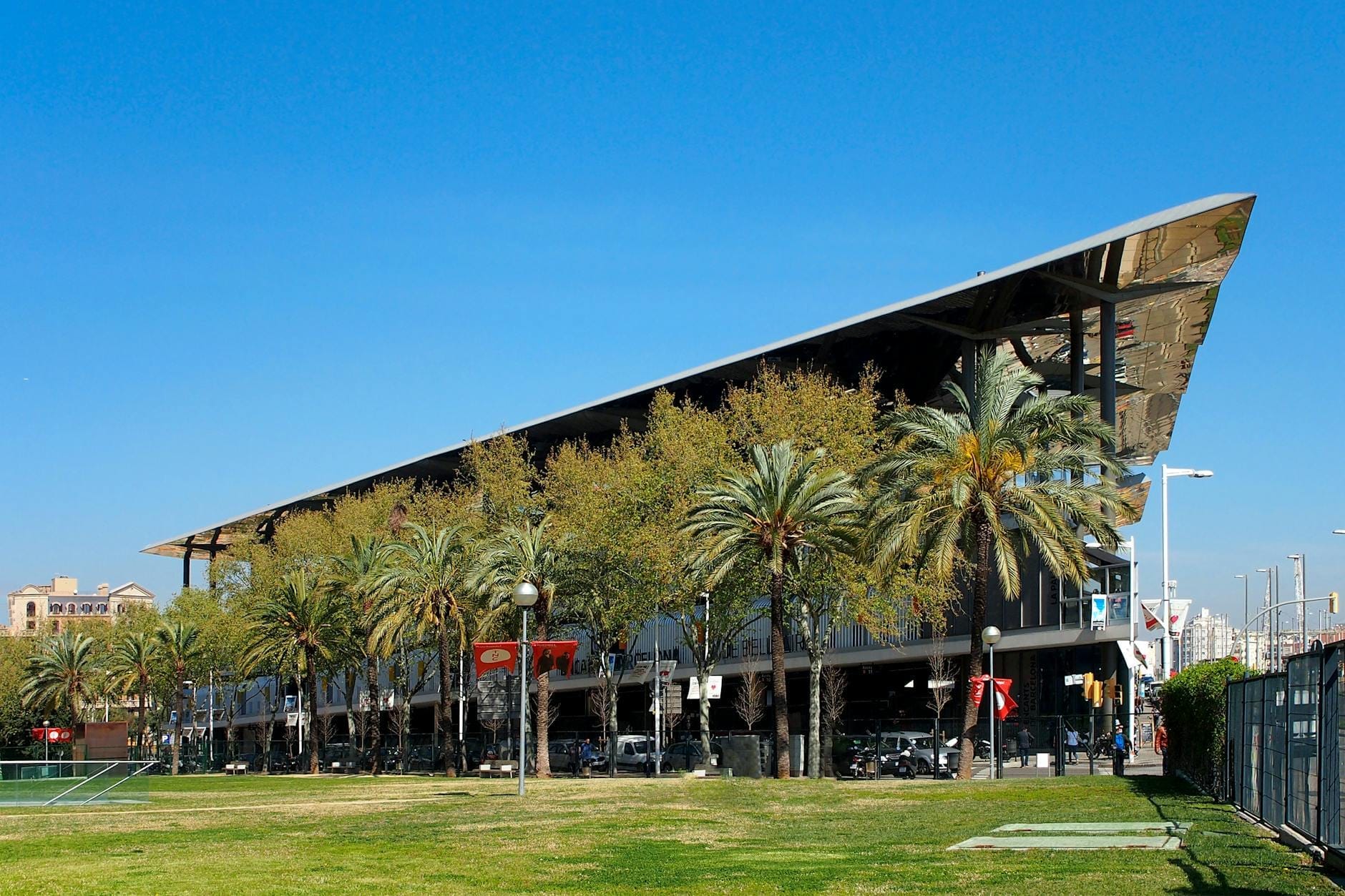 Modern market building with a dramatic angled roof and palm trees in Barcelona, under a clear blue sky.