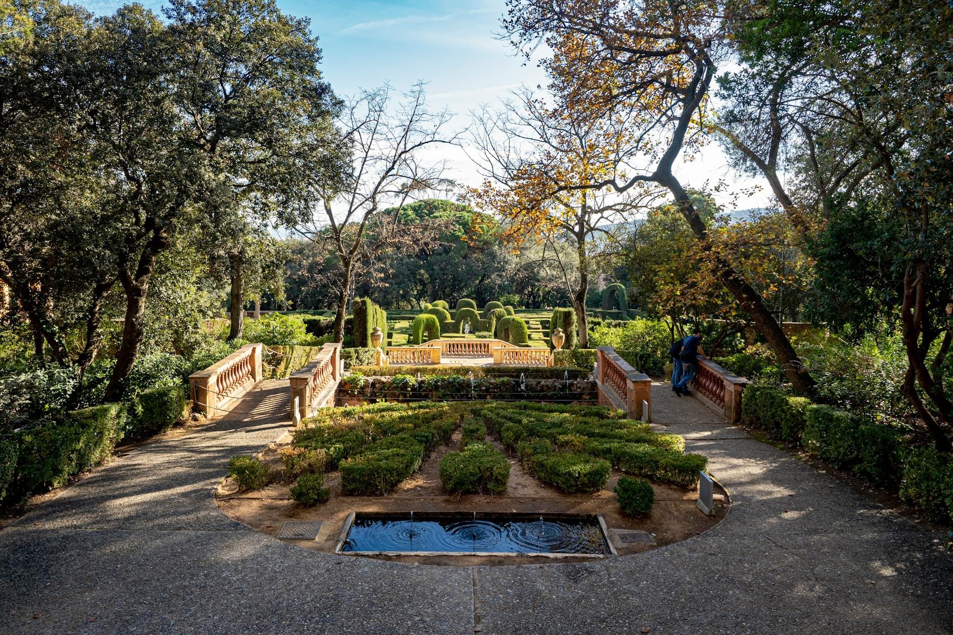 Sunlit view of green garden hedges, small fountain, and pathways in a leafy, less-crowded Barcelona park