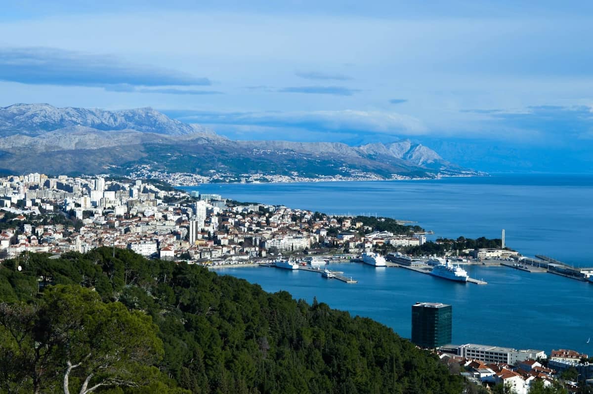 Panoramablick auf Split von einem erhöhten Aussichtspunkt auf dem Marjan-Hügel, mit Blick auf die Stadt, den Hafen, das Meer und einen üppigen Kiefernwald im Vordergrund.