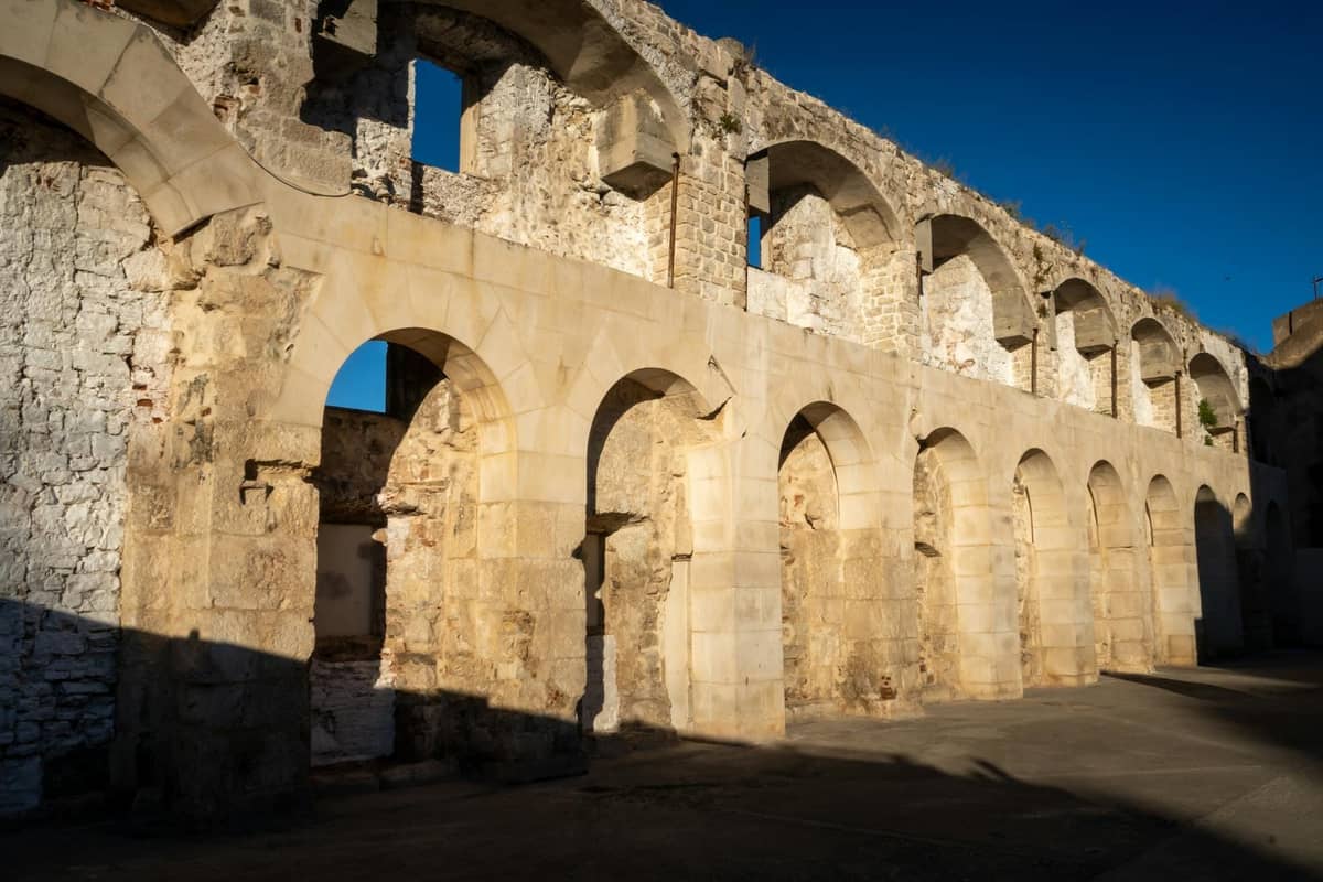 Teilweise erhaltene römische Steinmauern mit Bögen in starkem Sonnenlicht, die antike Ruinen außerhalb des Diokletianspalastes in Split, Kroatien, zeigen.