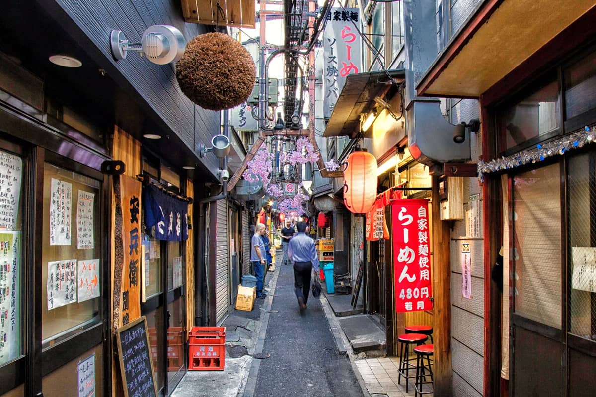 Narrow atmospheric alleyway in Tokyo lined with tiny ramen shops, colorful lanterns, and hanging signs, capturing a hidden local dining spot.