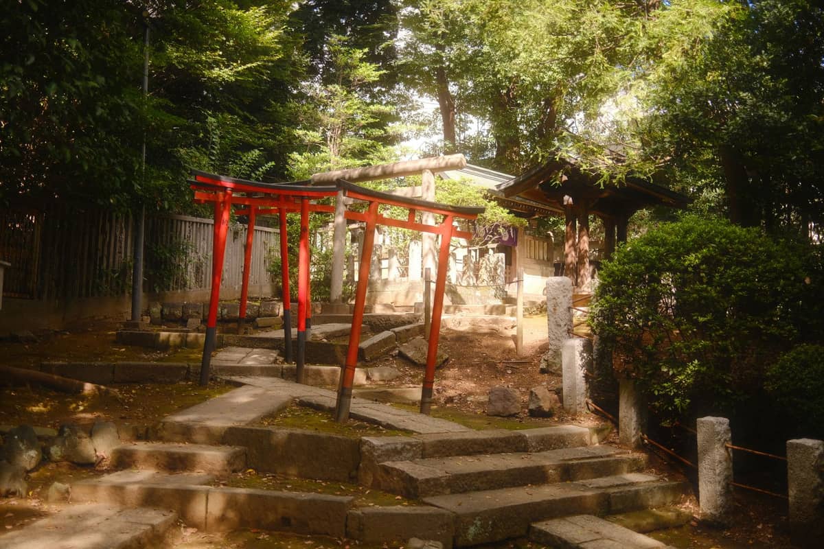 A small, red torii gate and stone steps lead to a secluded shrine tucked in the trees, creating a peaceful, hidden atmosphere.
