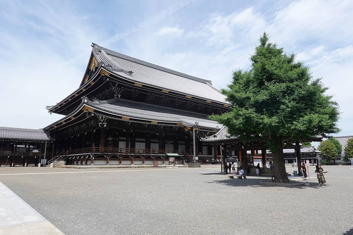 Wide-angle view of the grand Founder's Hall (Miei-dō) and Amida Hall at Higashi Hongan-ji, Kyoto, with open courtyard and visitors under a large tree.