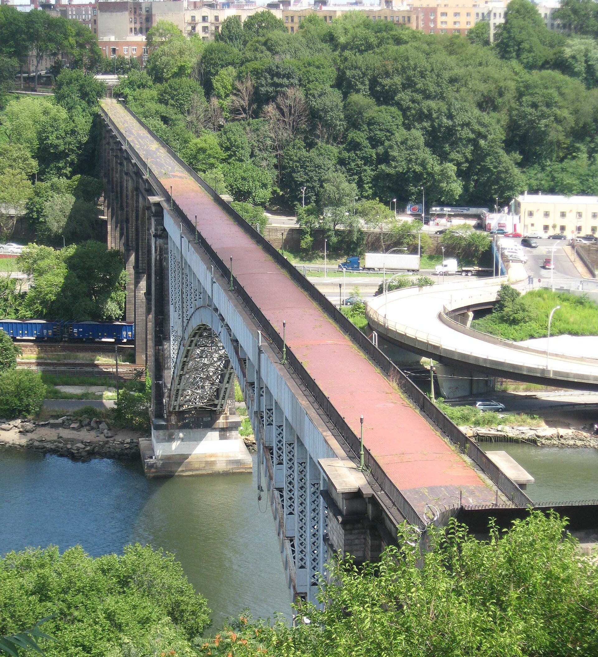 Il High Bridge che attraversa il Harlem River, circondato da rigogliosi alberi verdi e edifici cittadini sotto la luce del giorno a New York City.