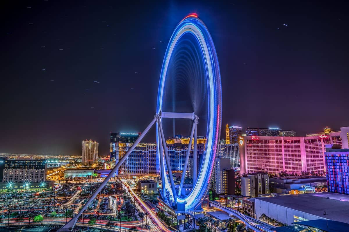 La noria de observación High Roller de Las Vegas, brillantemente iluminada de noche, se eleva sobre el horizonte de la ciudad con luces de colores y los edificios circundantes.