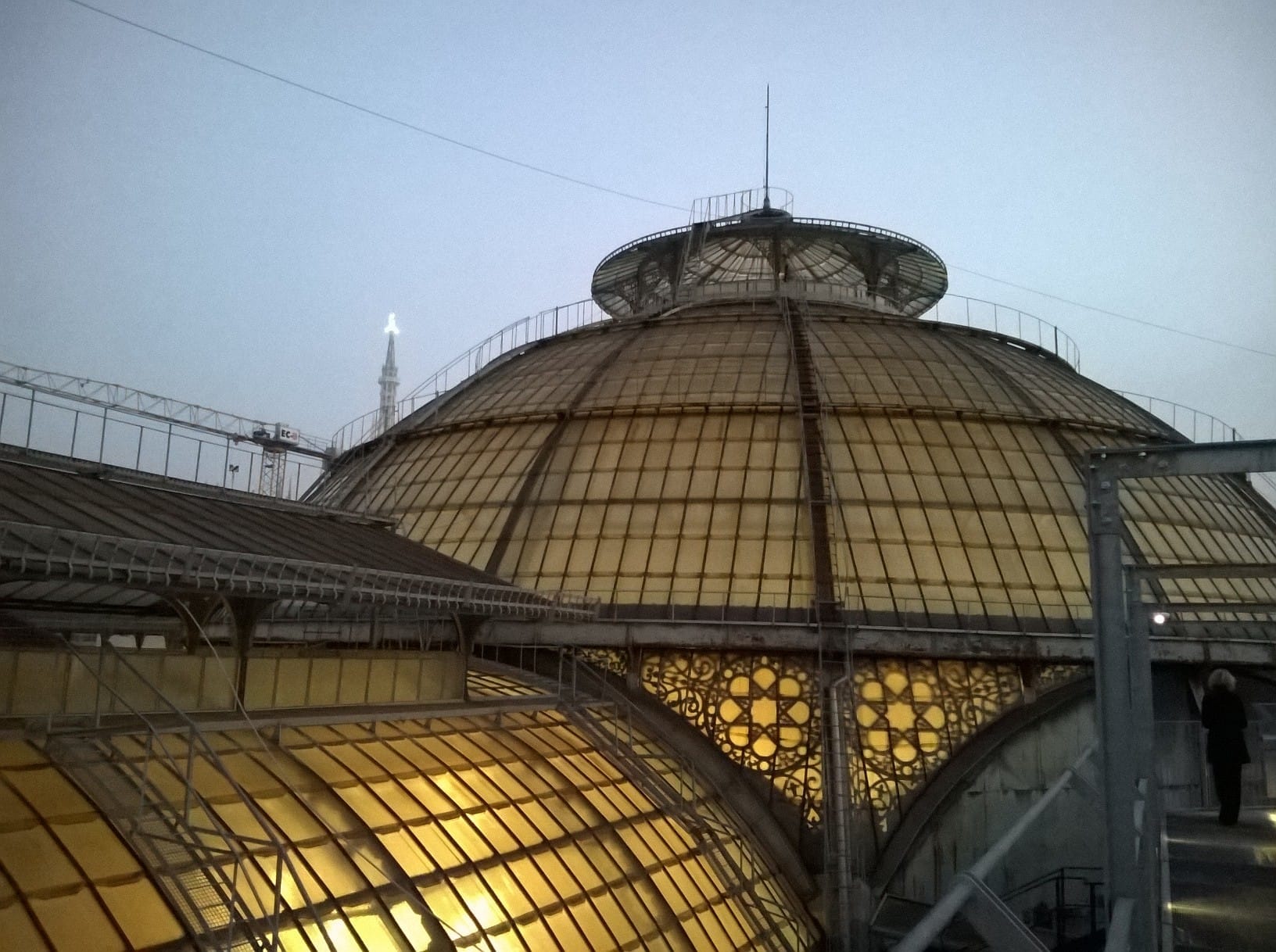 Il tetto in vetro a cupola della Galleria Vittorio Emanuele II al crepuscolo, visto dal camminamento della Highline Galleria, con le luci della città in sottofondo.