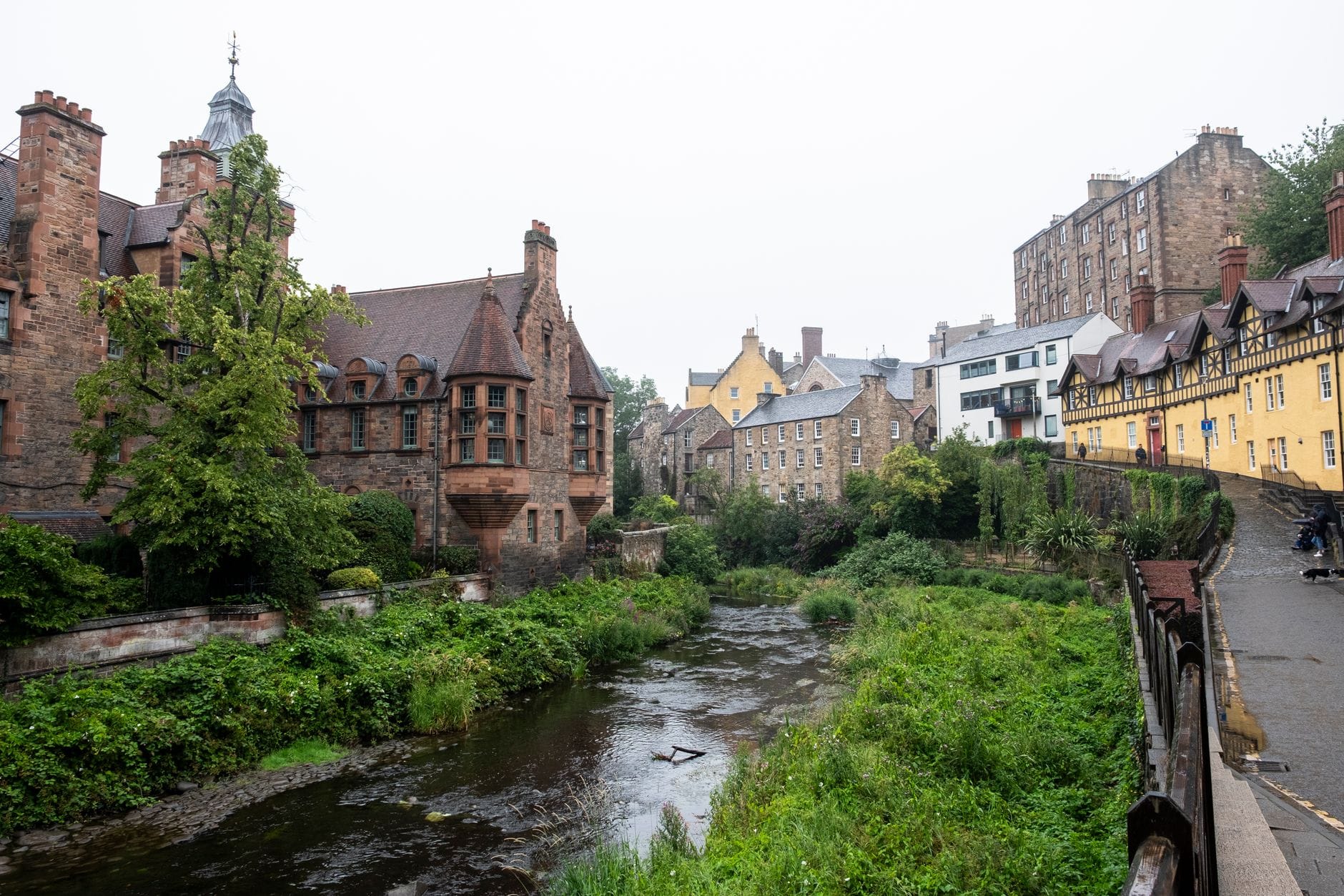 Fluss entlang der historischen Cottages von Dean Village und Grünflächen in Edinburgh, mit einem flachen Uferpfad auf der rechten Seite.