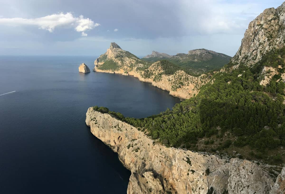 Dramatische Küste mit steilen Felsklippen und grünen Hügeln, die nahe der Halbinsel Formentor im Norden Mallorcas unter einem bewölkten Himmel auf das Meer treffen.