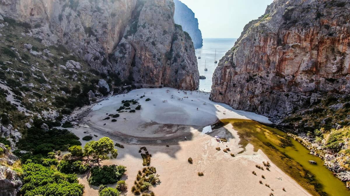 Dramatische Kalksteinschlucht mit Blick auf das Meer, senkrechten Klippen, einem Sandbereich und einem Bach – wahrscheinlich der ikonische Sa Calobra Canyon auf Mallorca.
