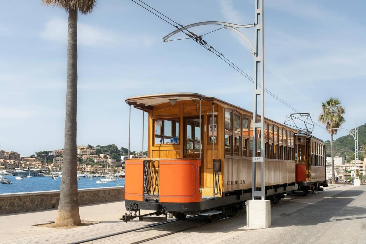 Historische Holzstraßenbahn am Meer in Port de Sóller, Mallorca, mit Bergen und Dorf im Hintergrund.