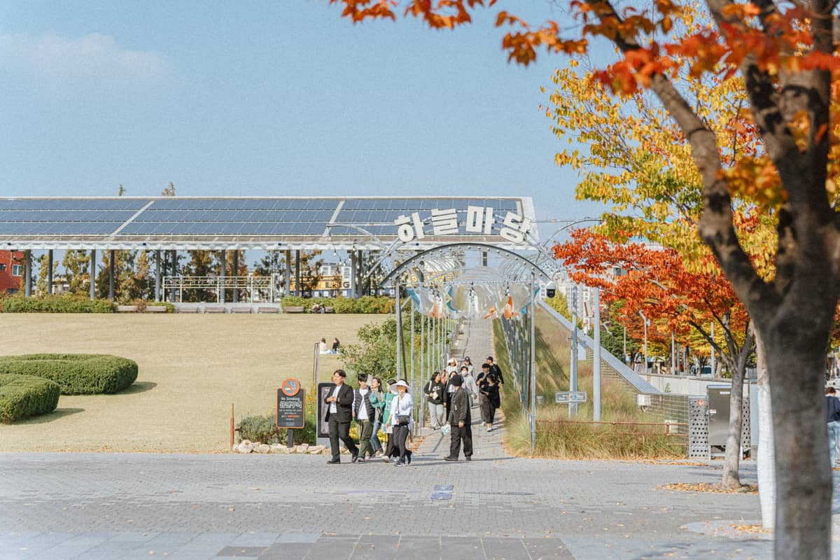 Pessoas caminhando em direção ao Haneul Park, um popular parque no topo de uma colina em Seul, com árvores de outono e céu azul limpo.